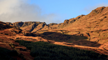 Looking up at a ridge illuminated by evening light, partly covered by a cloud shadow